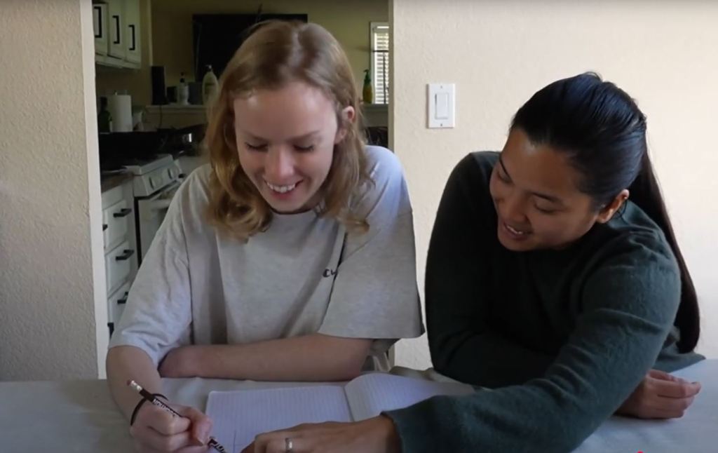 Student smiling while working in a notebook as an executive function tutor provides guidance, both engaged in collaborative learning—illustrating a supportive and encouraging tutoring session.